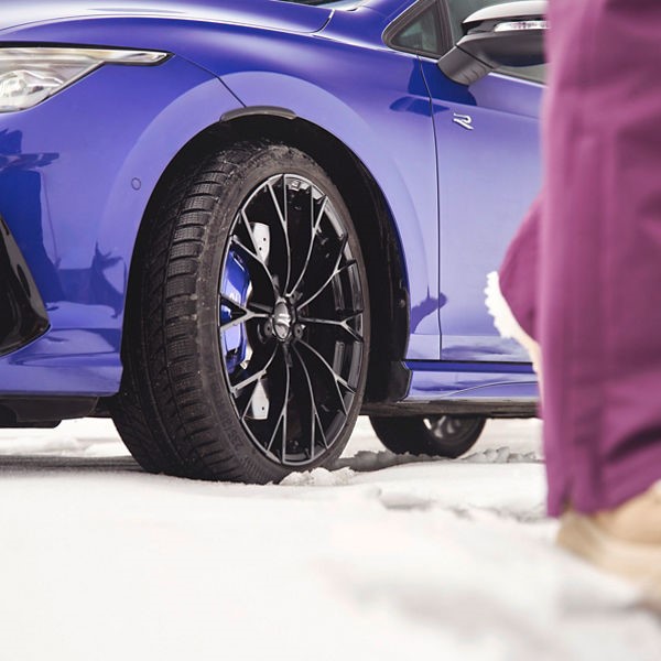 Blue VW R on snow, focusing on the front wheel with winter tyre.